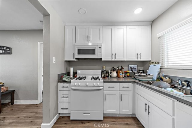 kitchen with white appliances, a sink, white cabinets, dark wood-style flooring, and baseboards