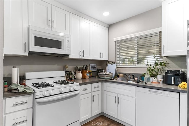 kitchen featuring white appliances, a sink, dark countertops, white cabinets, and recessed lighting