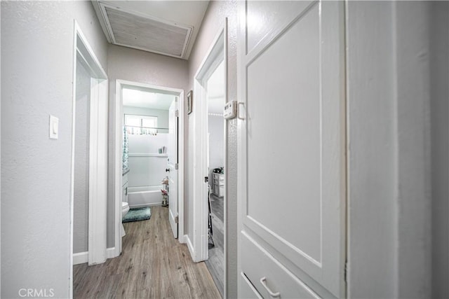 hallway with light wood-type flooring, attic access, baseboards, and a textured wall