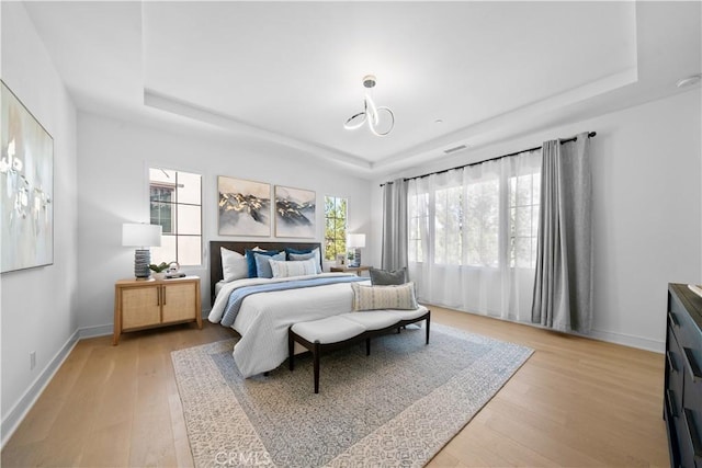 bedroom featuring baseboards, light wood finished floors, and a raised ceiling