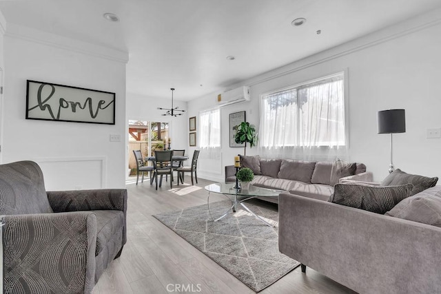 living room featuring baseboards, a wall unit AC, light wood finished floors, and a chandelier