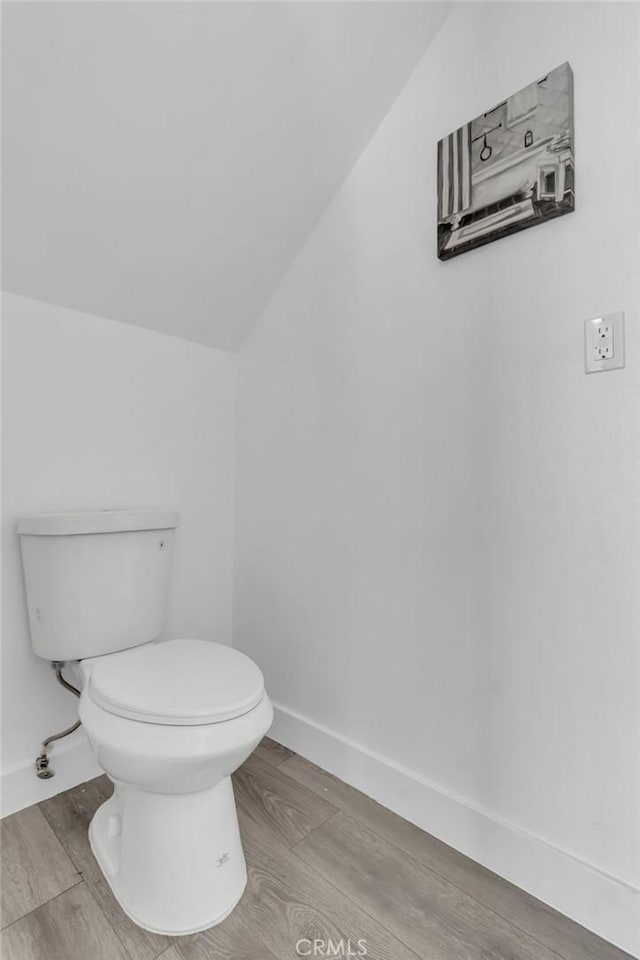 bathroom with baseboards, lofted ceiling, wood finished floors, and toilet