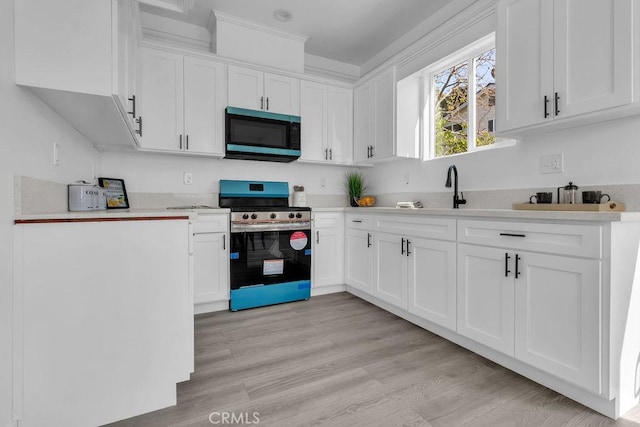 kitchen with electric range, light countertops, a sink, white cabinets, and light wood-style floors