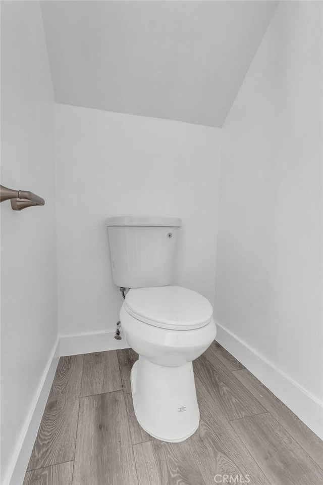 bathroom with toilet, baseboards, vaulted ceiling, and wood finished floors