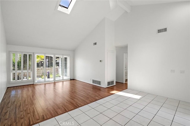 empty room featuring high vaulted ceiling, visible vents, a skylight, and beam ceiling