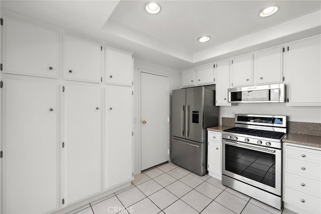 kitchen with stainless steel appliances, recessed lighting, white cabinetry, light tile patterned floors, and a tray ceiling