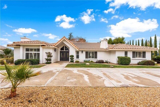 mediterranean / spanish-style house featuring a chimney, a tile roof, and stucco siding
