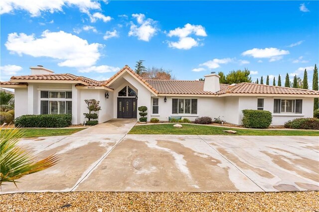 mediterranean / spanish house with a tiled roof, a chimney, stucco siding, and a front yard
