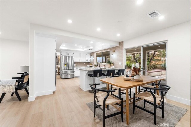 dining area with visible vents, light wood-type flooring, baseboards, a tray ceiling, and recessed lighting