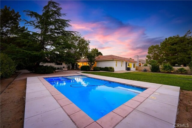 pool at dusk featuring a patio, an outdoor pool, and a yard