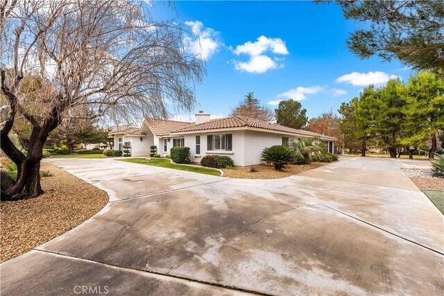 view of property exterior featuring driveway, a chimney, a tile roof, and stucco siding