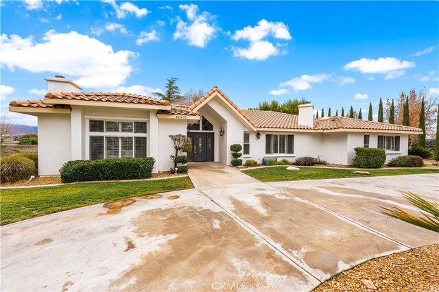 mediterranean / spanish home featuring a front lawn, stucco siding, and a chimney