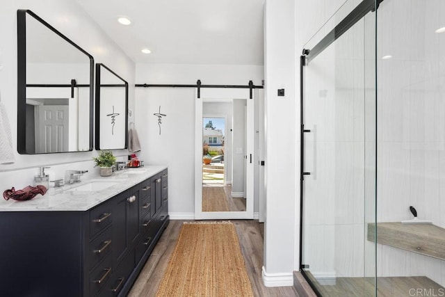 full bathroom with double vanity, a sink, wood finished floors, and a stall shower