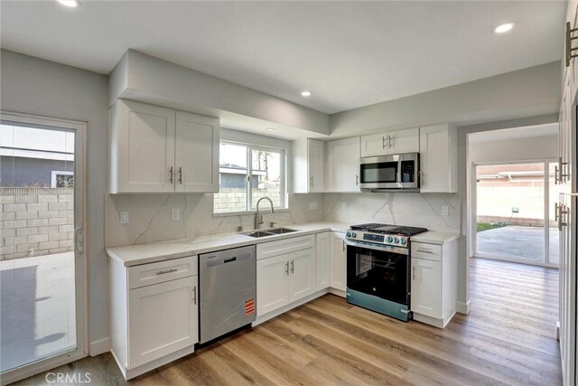 kitchen with white cabinetry, a sink, light wood finished floors, backsplash, and stainless steel appliances