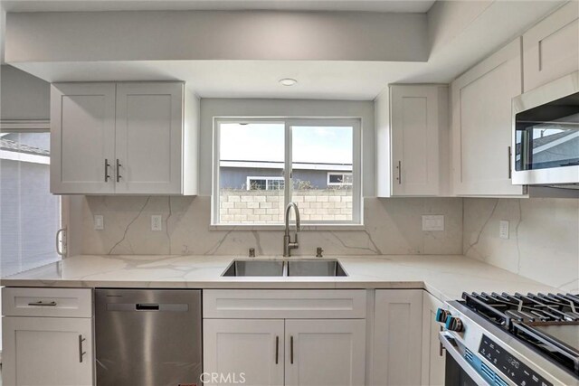kitchen featuring light stone counters, a sink, stainless steel appliances, white cabinetry, and backsplash