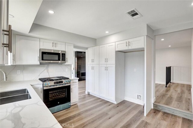 kitchen featuring white cabinets, light stone countertops, appliances with stainless steel finishes, a sink, and visible vents