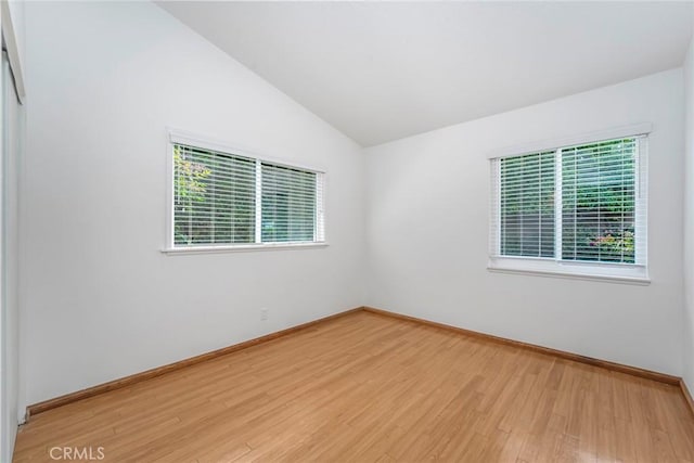 spare room with baseboards, vaulted ceiling, and light wood-style flooring