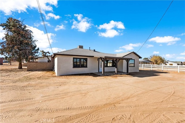 back of house with dirt driveway, stucco siding, and fence