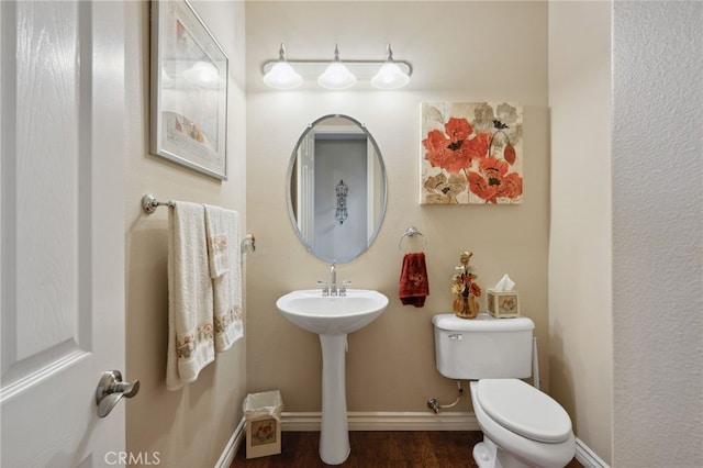 bathroom featuring baseboards, wood finished floors, and toilet
