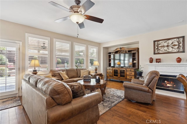 living room with a ceiling fan, a glass covered fireplace, and wood finished floors