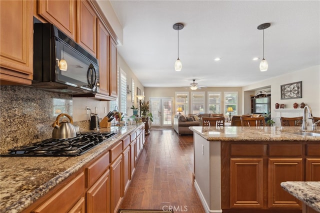 kitchen with backsplash, brown cabinets, a sink, black appliances, and open floor plan