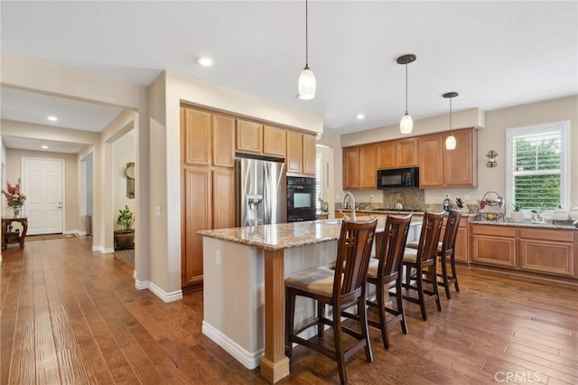 kitchen with a kitchen island with sink, light stone countertops, a breakfast bar area, dark wood-style floors, and black appliances