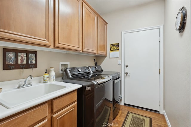 clothes washing area featuring wood finished floors, cabinet space, a sink, baseboards, and washer and dryer