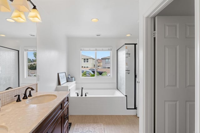 full bath featuring a sink, wood finished floors, a healthy amount of sunlight, a garden tub, and a stall shower