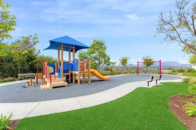 communal playground featuring a lawn, fence, and a mountain view