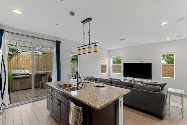 kitchen with a sink, light stone countertops, light wood-style flooring, and decorative light fixtures