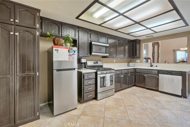 kitchen featuring dark brown cabinetry, light tile patterned flooring, light countertops, a sink, and appliances with stainless steel finishes