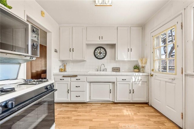 kitchen with decorative backsplash, white gas range, tile countertops, stainless steel microwave, and white cabinets