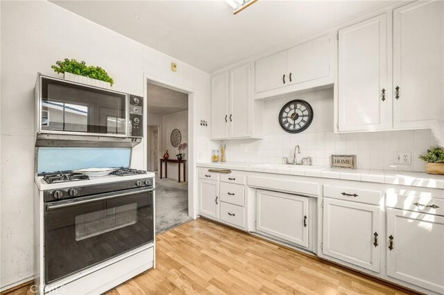kitchen with gas range gas stove, stainless steel microwave, white cabinets, a sink, and light wood-style flooring