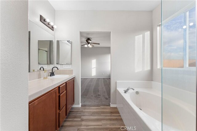 full bath featuring ceiling fan, a wealth of natural light, a garden tub, and vanity