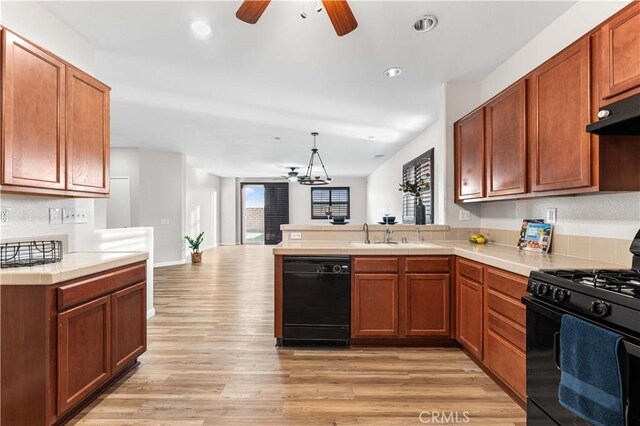 kitchen featuring light wood-type flooring, a sink, black appliances, a peninsula, and ceiling fan with notable chandelier