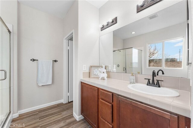 full bath with vanity, baseboards, a stall shower, and wood finished floors