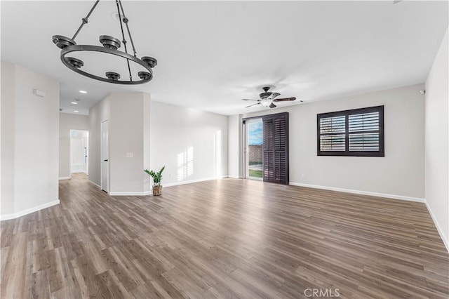 unfurnished living room featuring baseboards, wood finished floors, and ceiling fan with notable chandelier