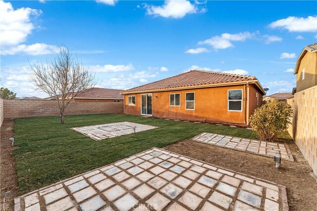 rear view of house with a fenced backyard, stucco siding, a patio area, a tiled roof, and a lawn