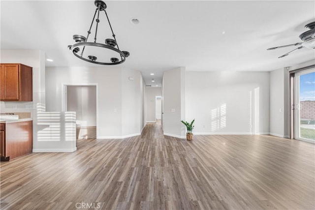 unfurnished living room with light wood-style floors, recessed lighting, baseboards, and ceiling fan with notable chandelier