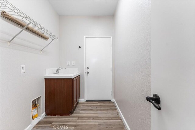 laundry area with light wood-type flooring, a sink, and baseboards
