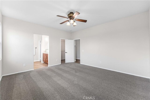 unfurnished bedroom with baseboards, ceiling fan, a spacious closet, carpet flooring, and ensuite bath