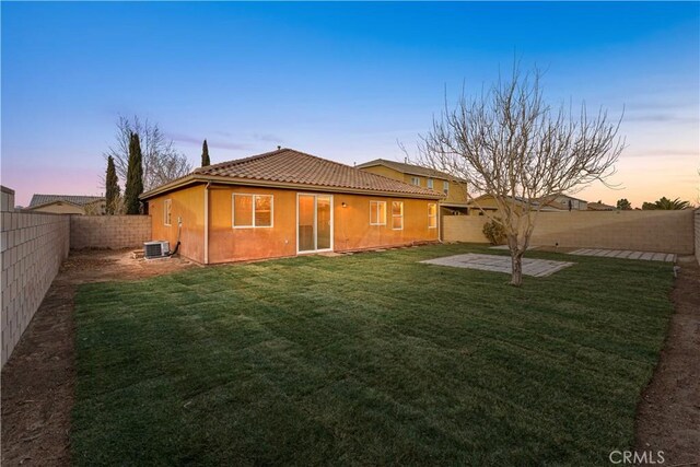 back of property at dusk with a patio, a fenced backyard, stucco siding, a tiled roof, and a lawn
