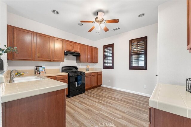kitchen with a ceiling fan, tile counters, under cabinet range hood, a sink, and gas stove