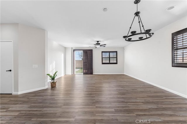 unfurnished living room featuring baseboards, ceiling fan with notable chandelier, and wood finished floors