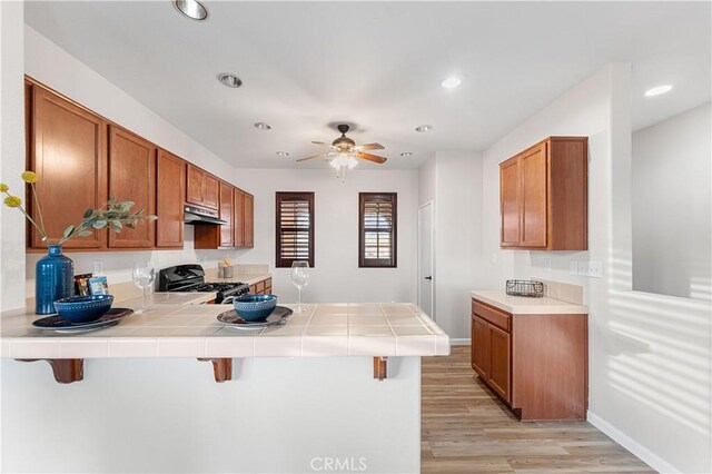 kitchen with light wood finished floors, a peninsula, brown cabinets, and gas range