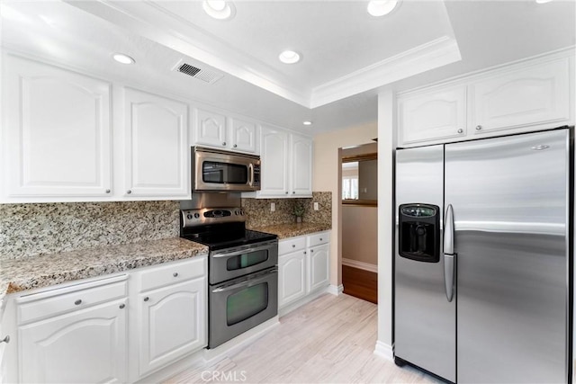kitchen featuring light wood-style floors, stainless steel appliances, white cabinetry, decorative backsplash, and a tray ceiling