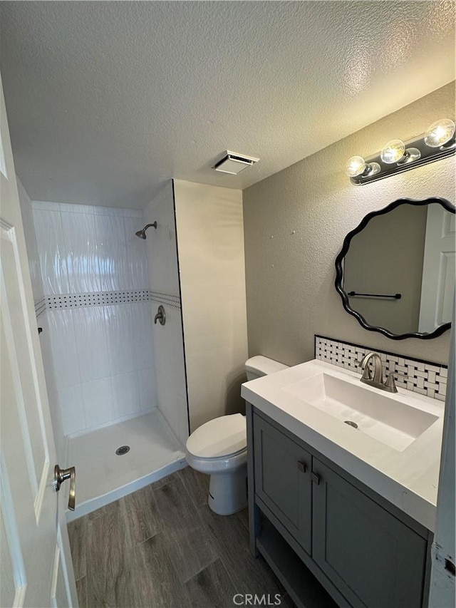 bathroom with vanity, toilet, a textured ceiling, wood finished floors, and tiled shower