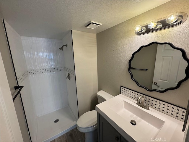 bathroom featuring vanity, toilet, a textured ceiling, visible vents, and tiled shower