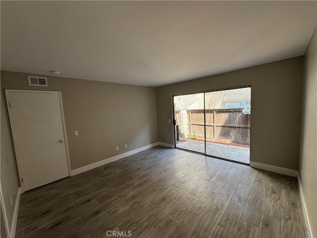 empty room featuring baseboards, dark wood-style flooring, and visible vents
