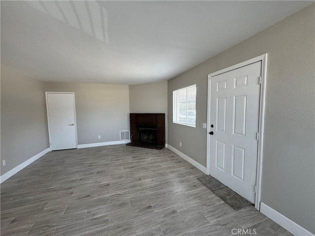 unfurnished living room featuring baseboards, a brick fireplace, wood finished floors, and visible vents